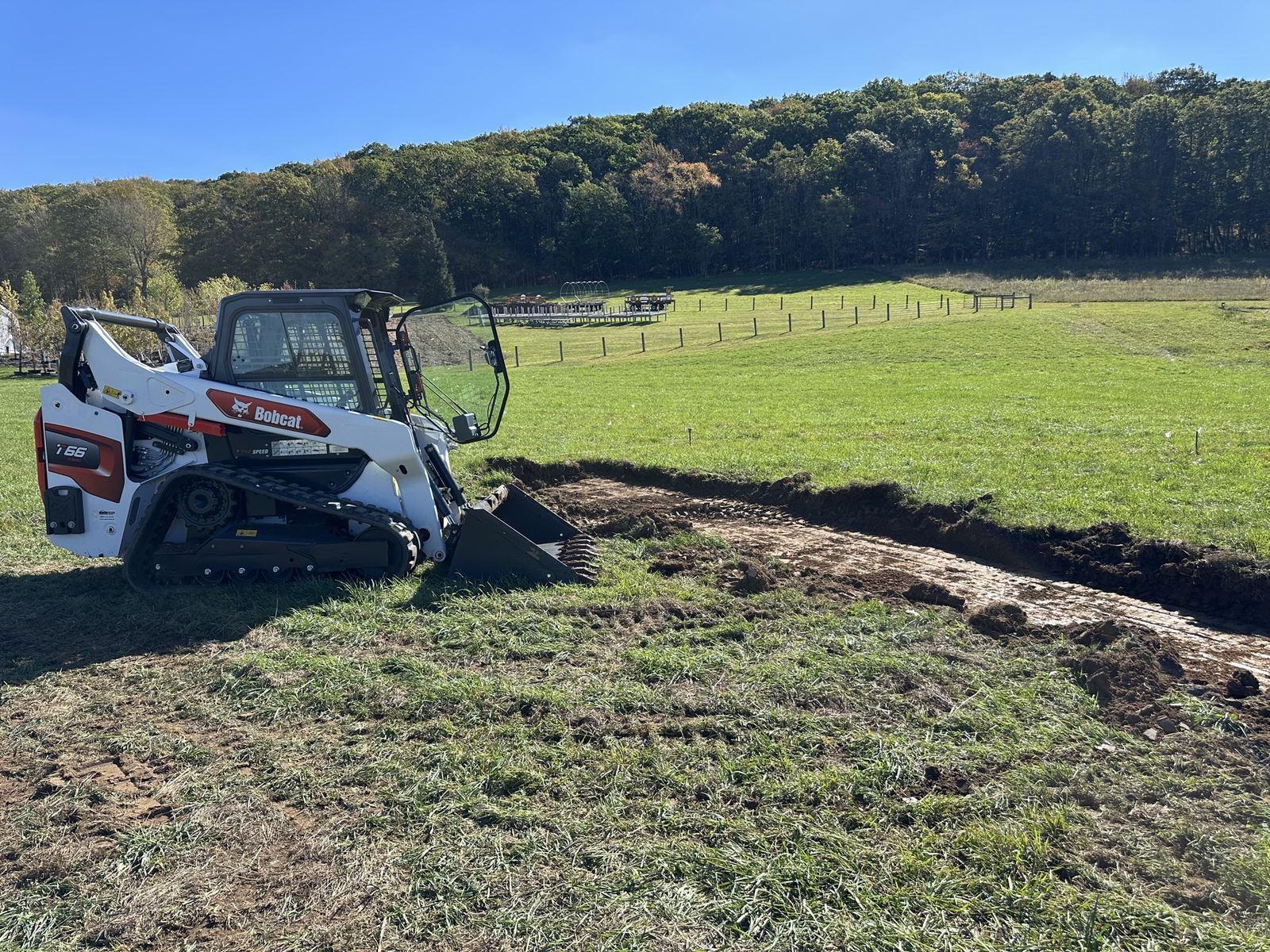 A Bobcat T66 cutting a utility trench across the pasture at Green Meadow.