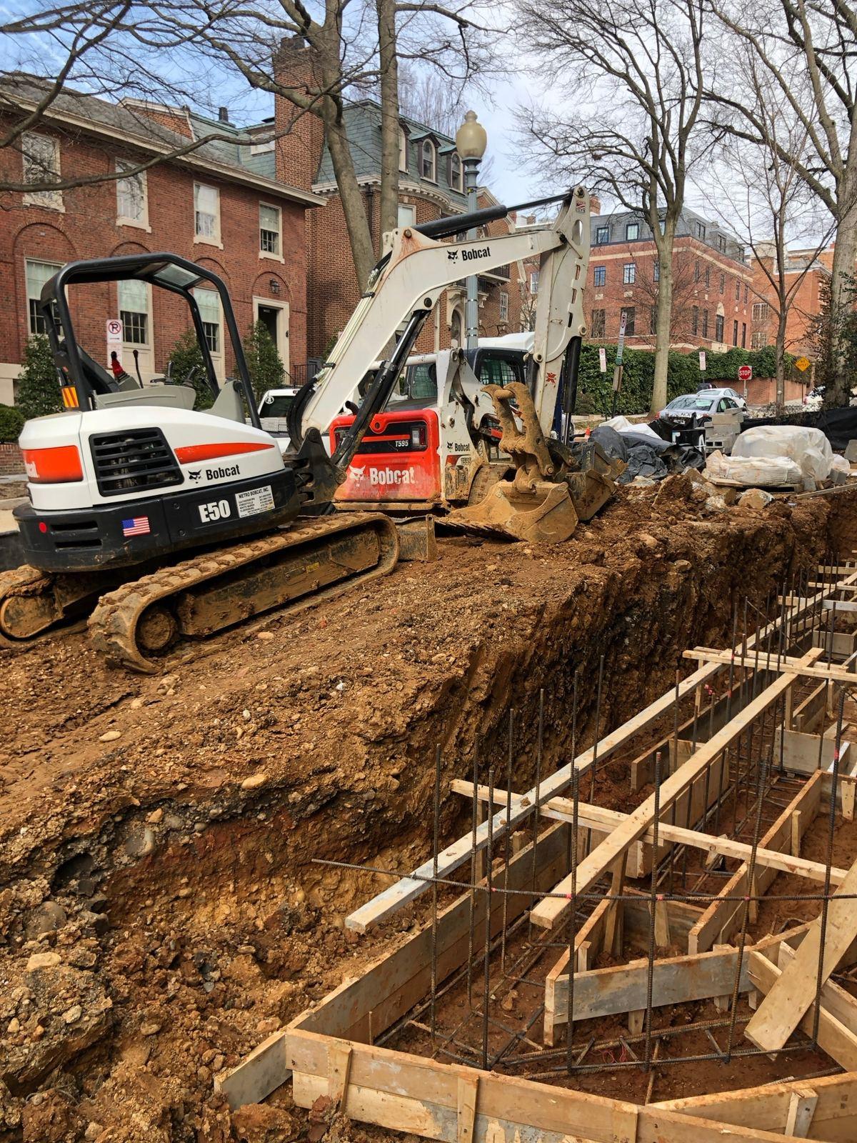 A Bobcat excavator digging a foundation beside footing forms.
